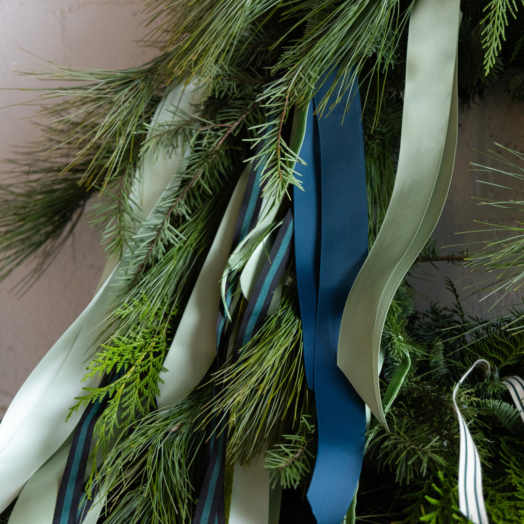 Decorative wreath with greenery and ribbons on a plain background