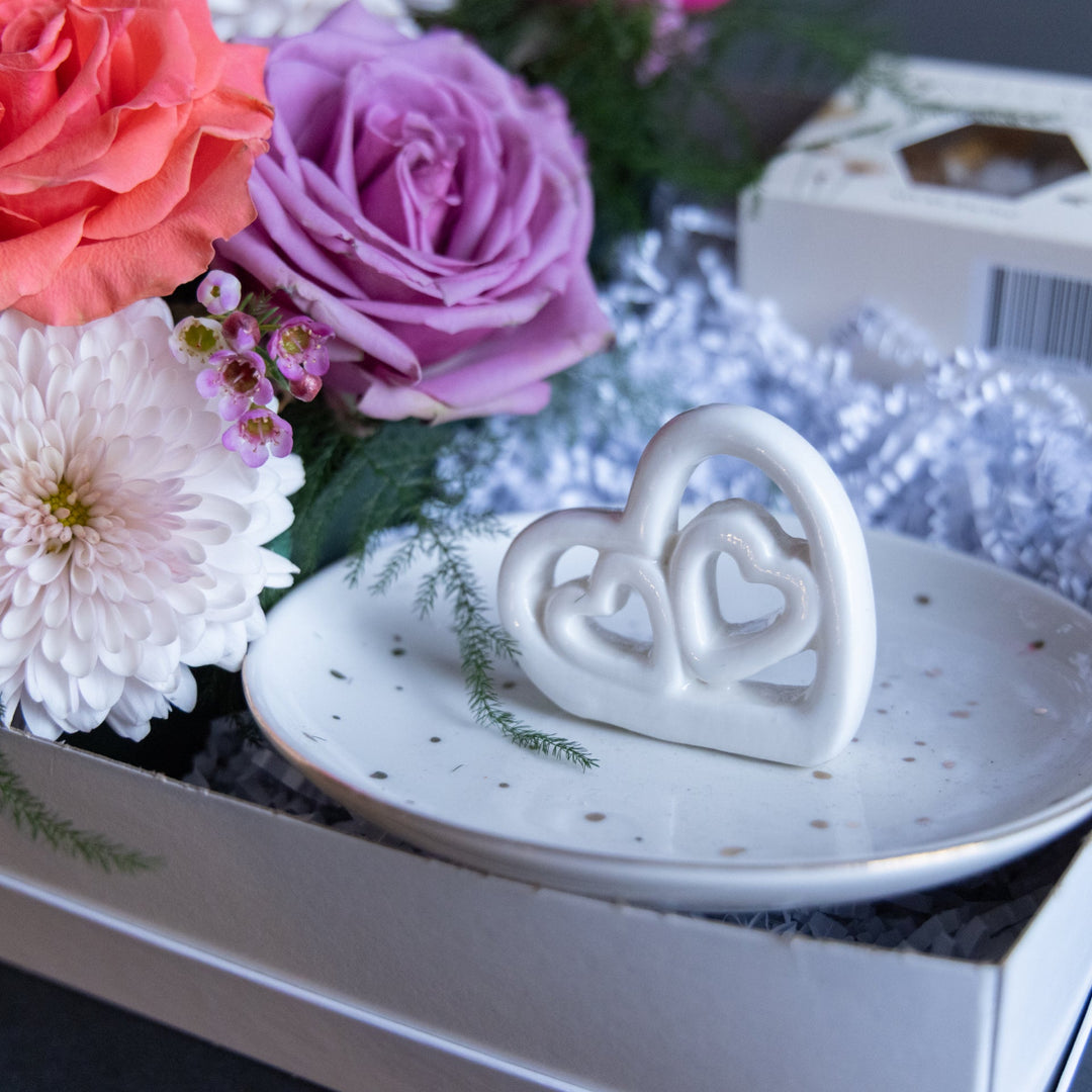 White ceramic heart-shaped object on a decorative plate with flowers in the background
