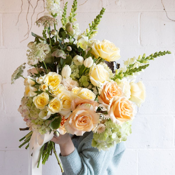 Bouquet of yellow, orange, and white flowers held by a person against a light background