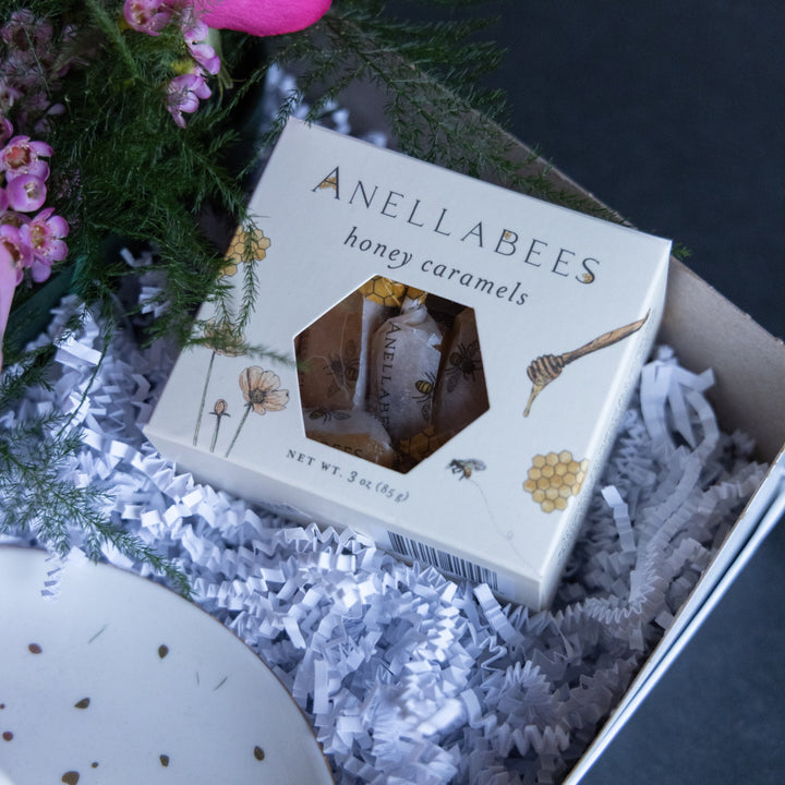 Box of Anellabees honey caramels with flowers and a decorative item in the background
