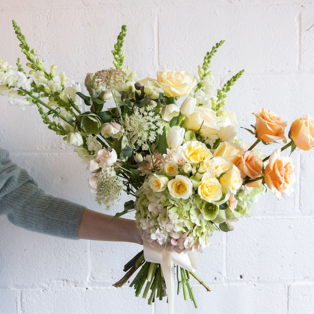 Bouquet of flowers held by a person against a white brick wall