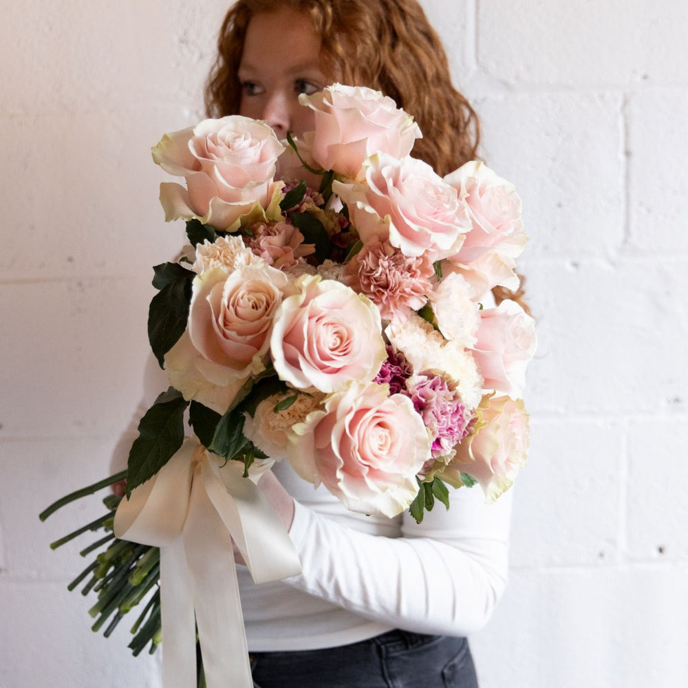 Person holding a bouquet of pink flowers against a white brick wall.