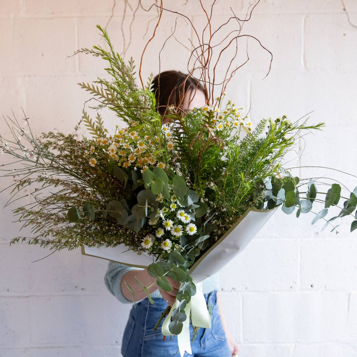 Person holding a large bouquet of greenery and flowers against a white background