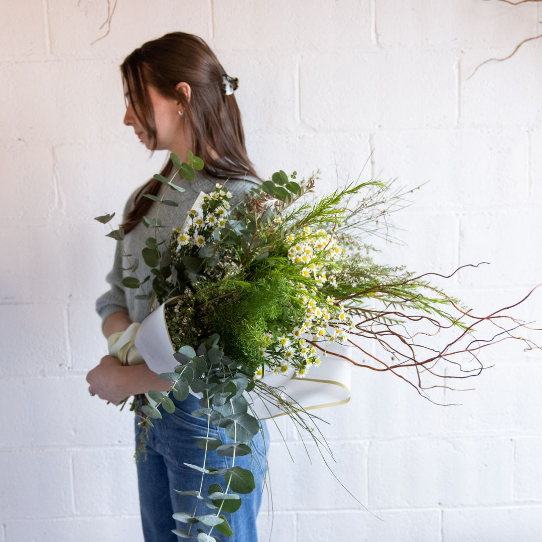 Person holding a bouquet of flowers against a white brick wall