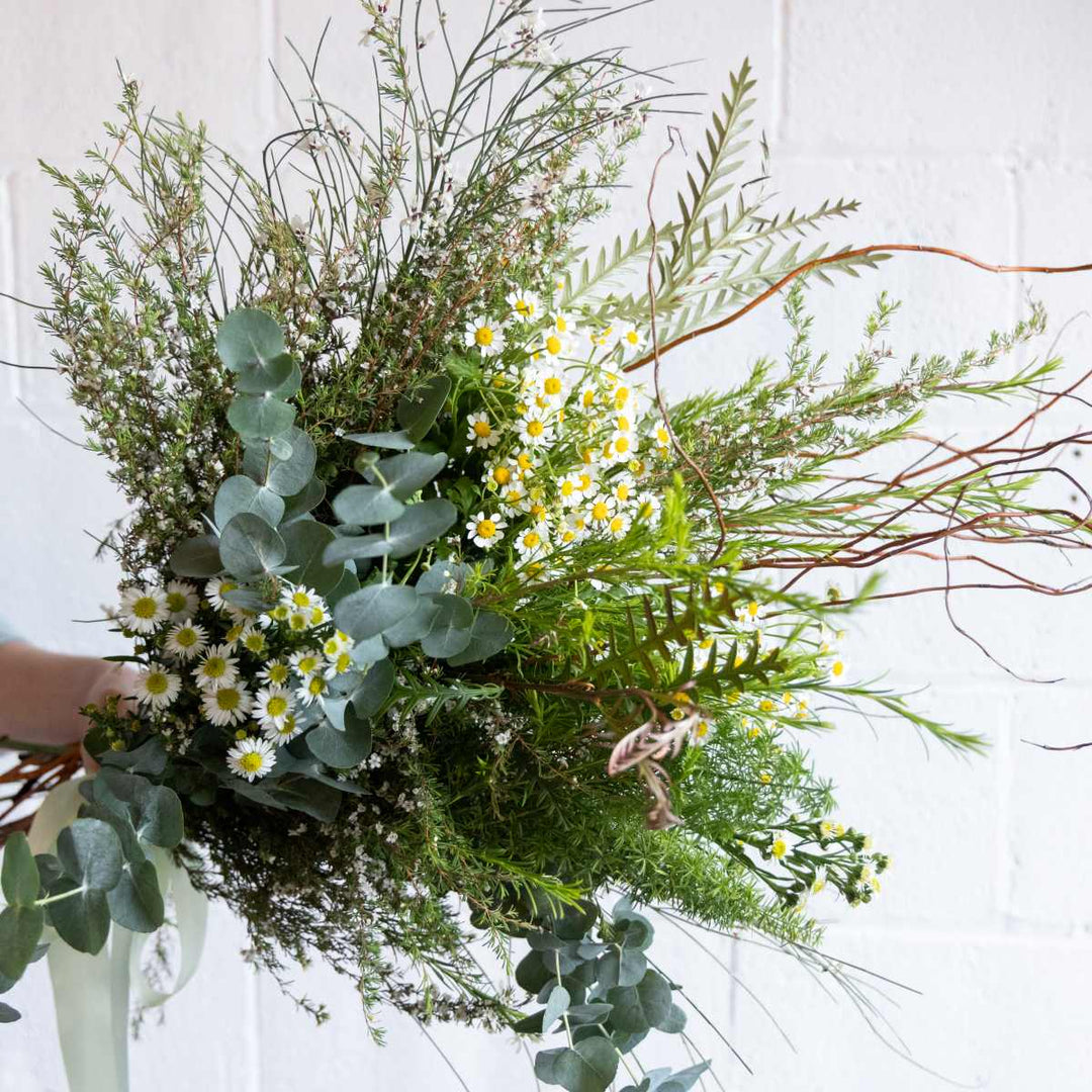 Bouquet of greenery and flowers held by a person against a white background