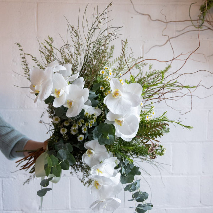 Bouquet of white flowers and greenery held by a person against a light background