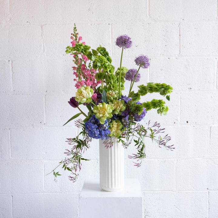 Bouquet of colorful flowers in a white vase against a white brick wall.