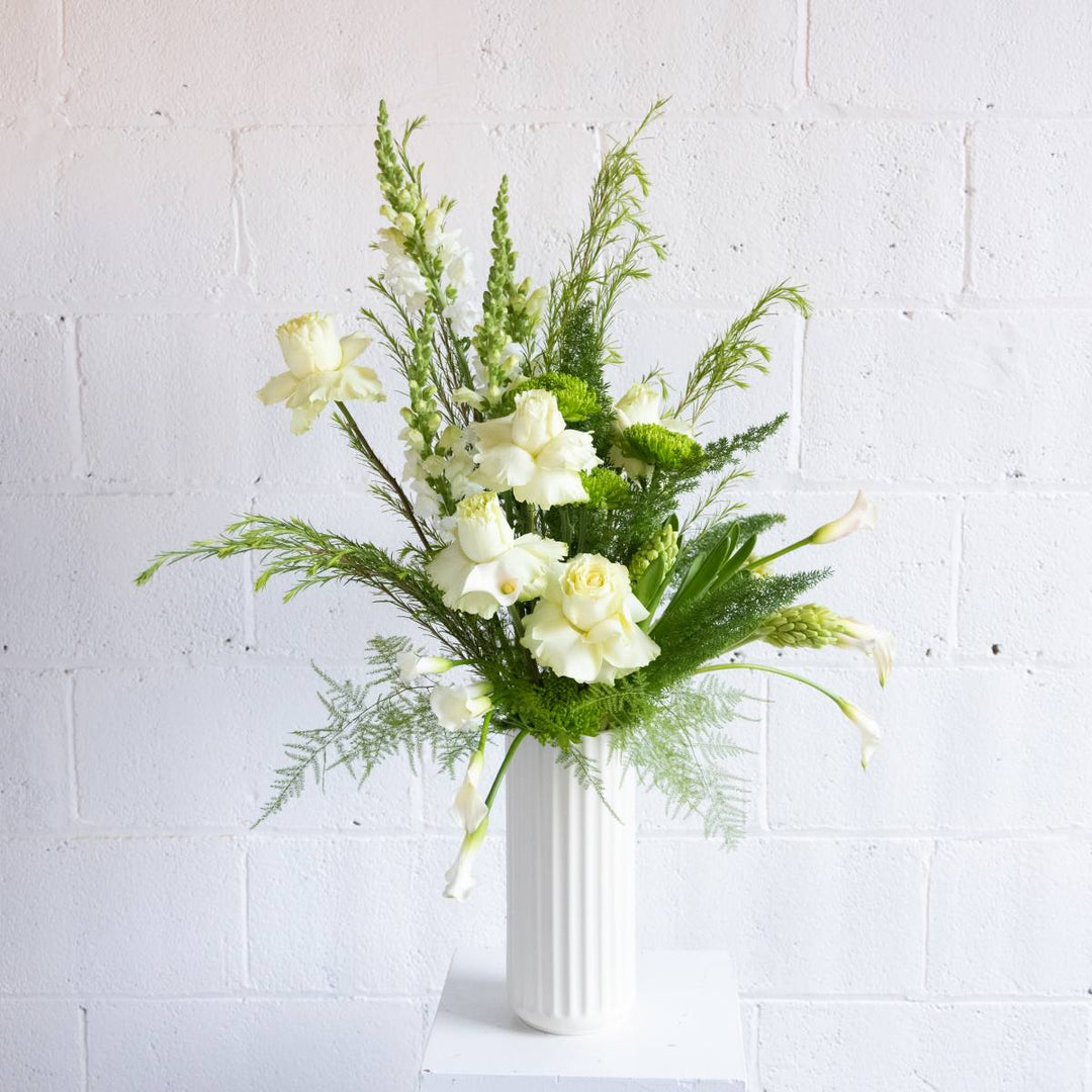Bouquet of white flowers and greenery in a white vase against a light gray background
