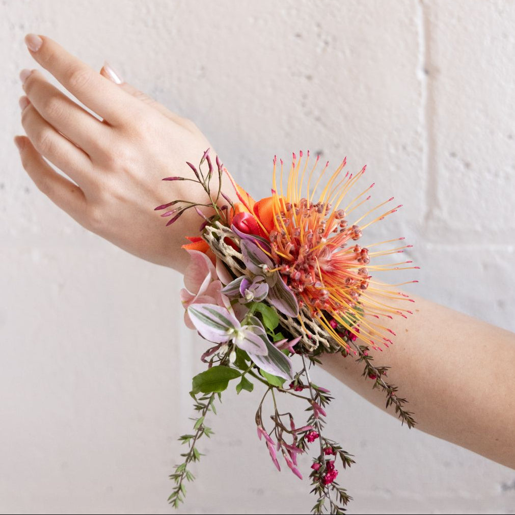Hand wearing a colorful floral wrist corsage against a light background