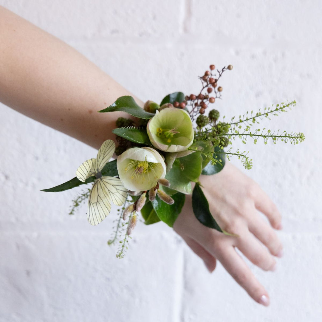 Hand wearing a green floral wrist corsage against a white background