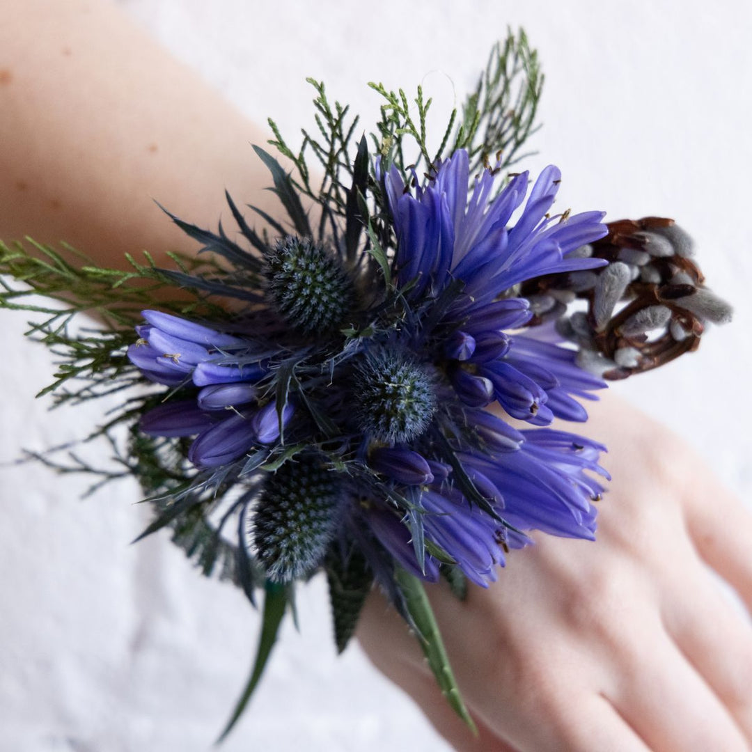 Close-up of a wrist corsage with purple flowers and greenery on a blurred background