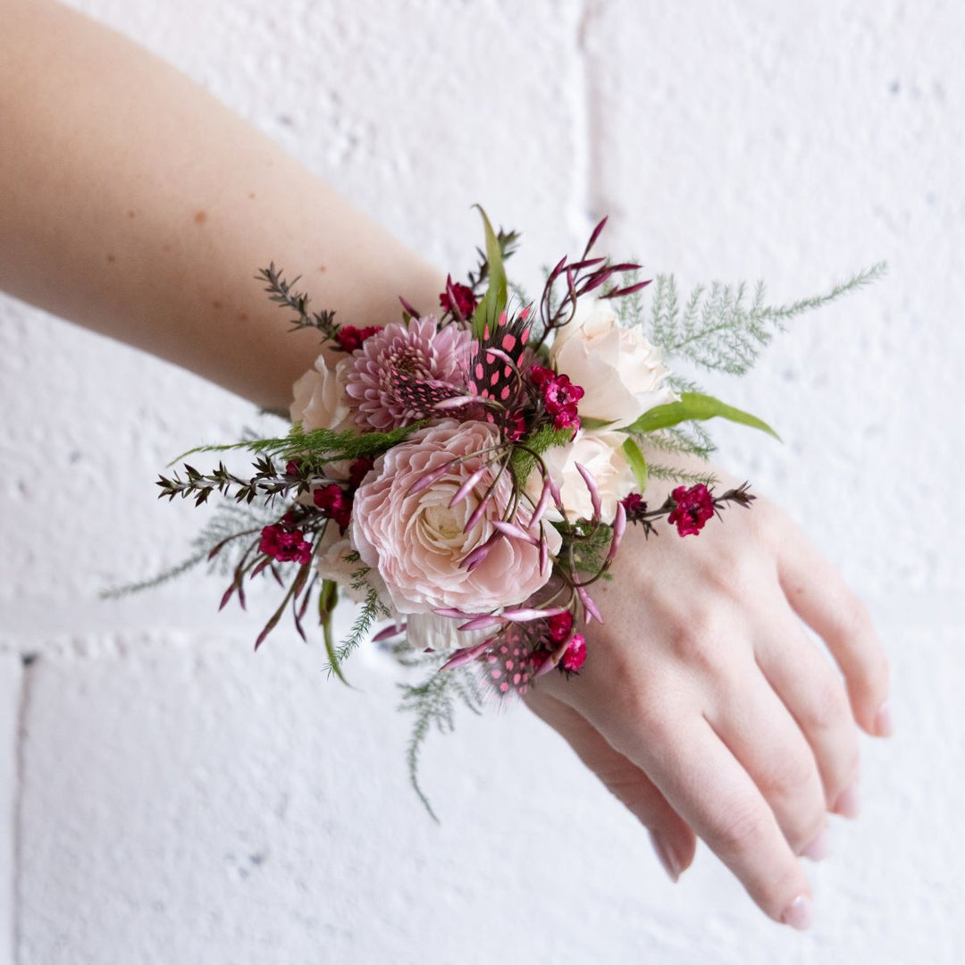 Hand wearing a floral wrist corsage against a light background