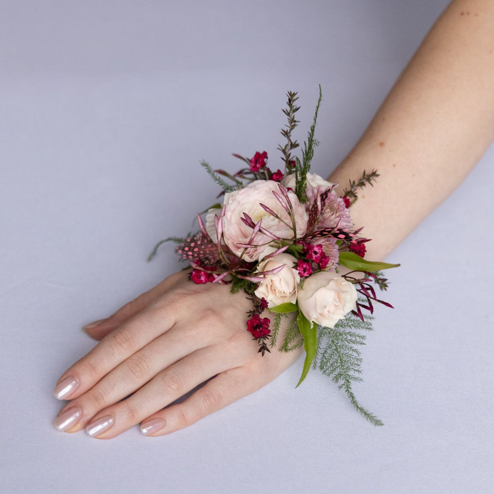 Floral wrist corsage on a person's wrist against a plain background