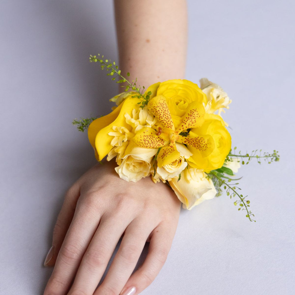 Yellow floral wrist corsage on a person's wrist against a light gray background