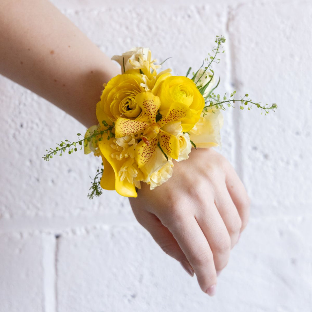Yellow floral wrist corsage on a person's wrist against a white background