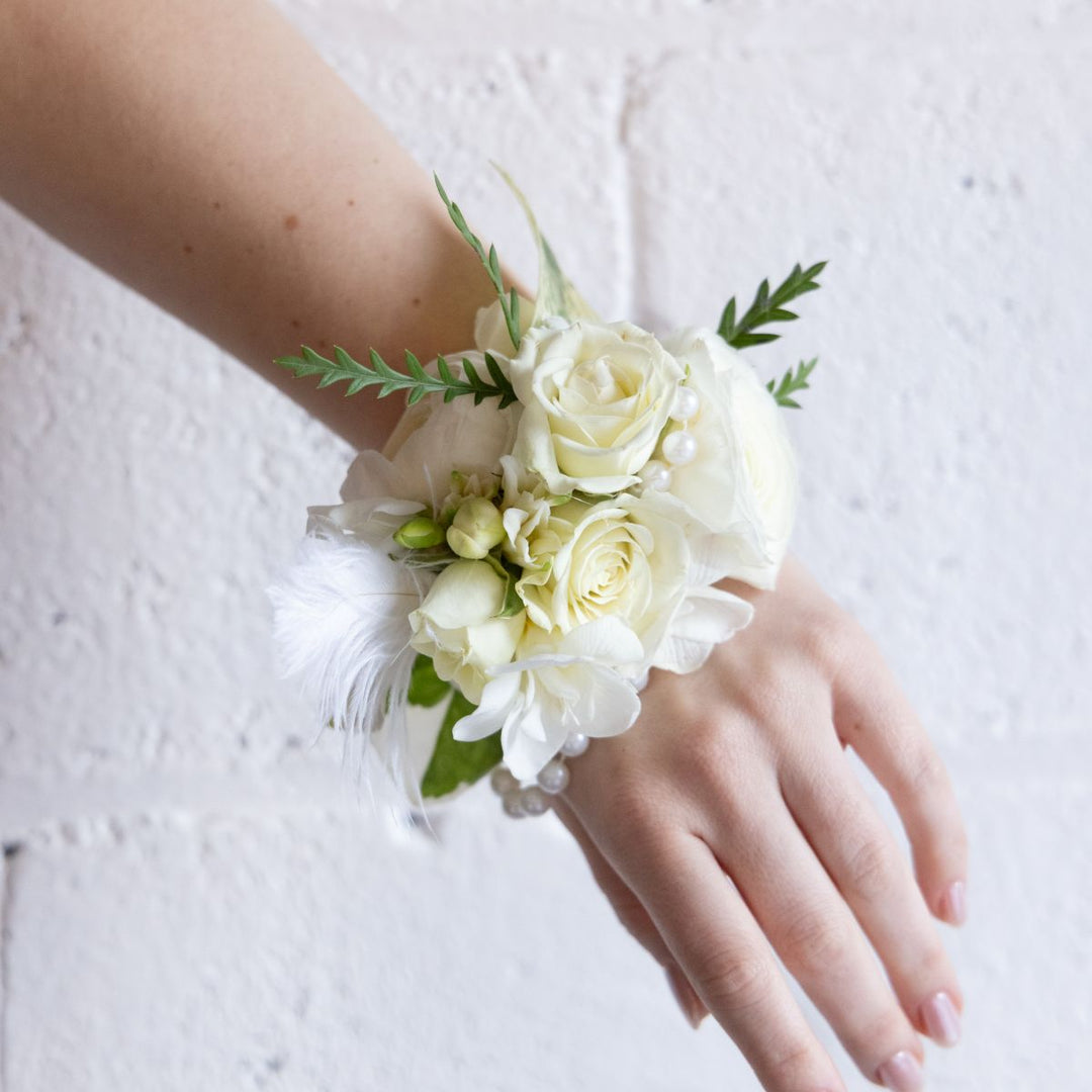 White floral wrist corsage on a person's wrist against a light background