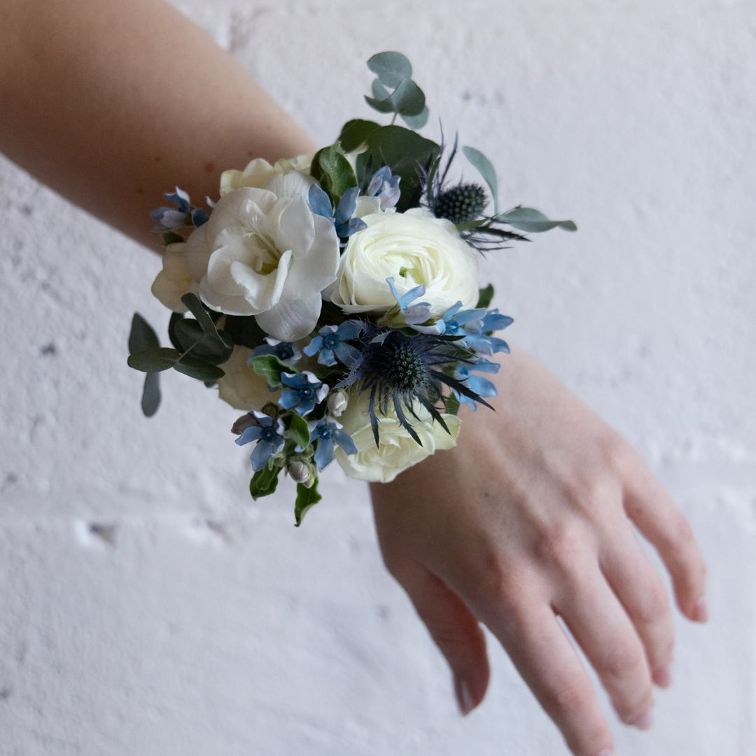 Floral wrist corsage with white and blue flowers on a person's wrist against a light background