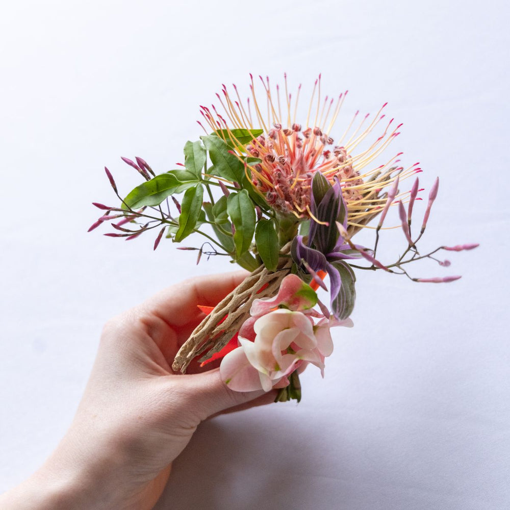 Hand holding a boutonniere against a light background