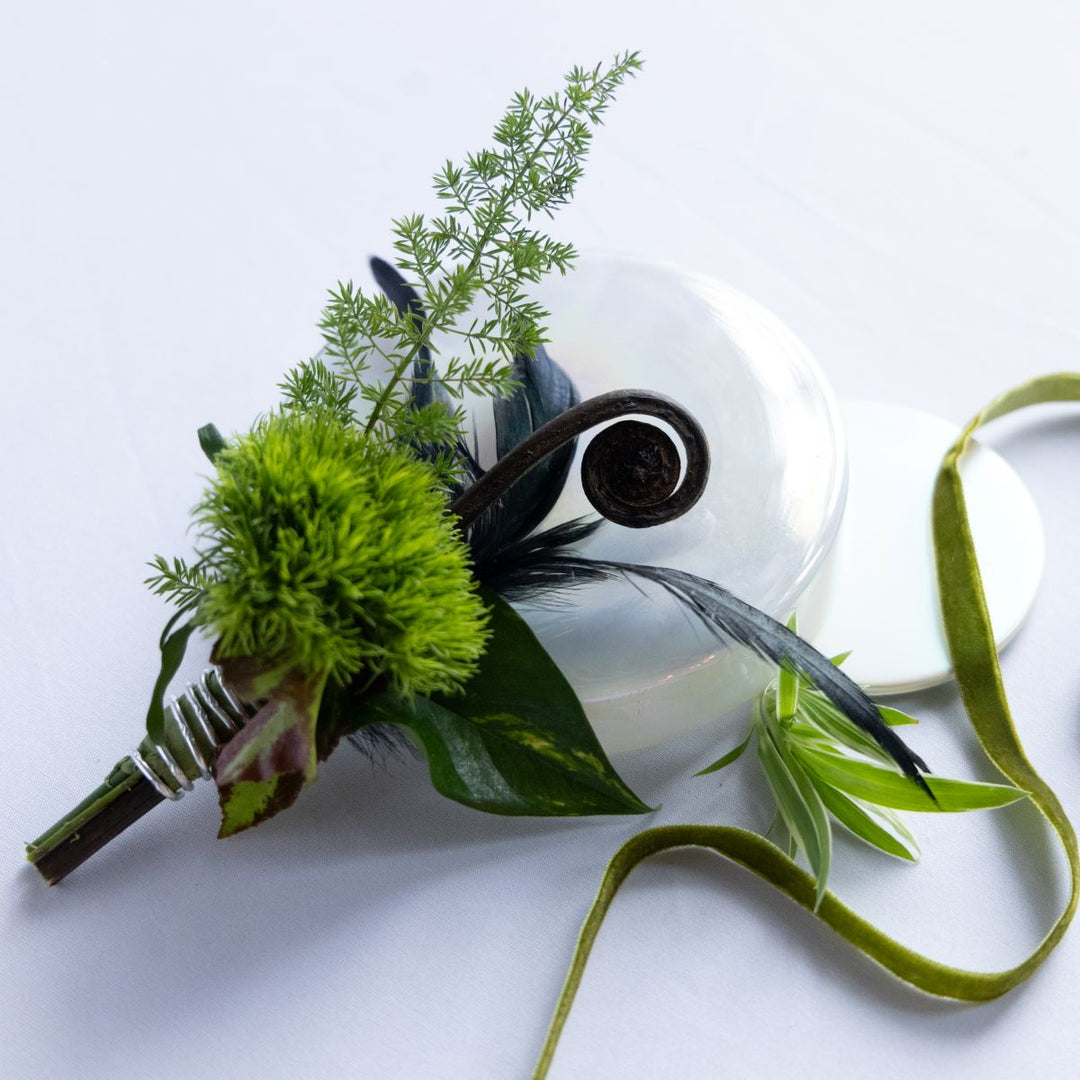 Green boutonniere with leaves and feathers on a white background