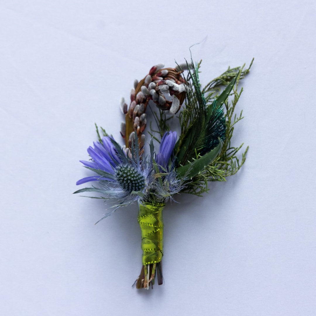 Floral boutonniere with purple flower and greenery on a white background