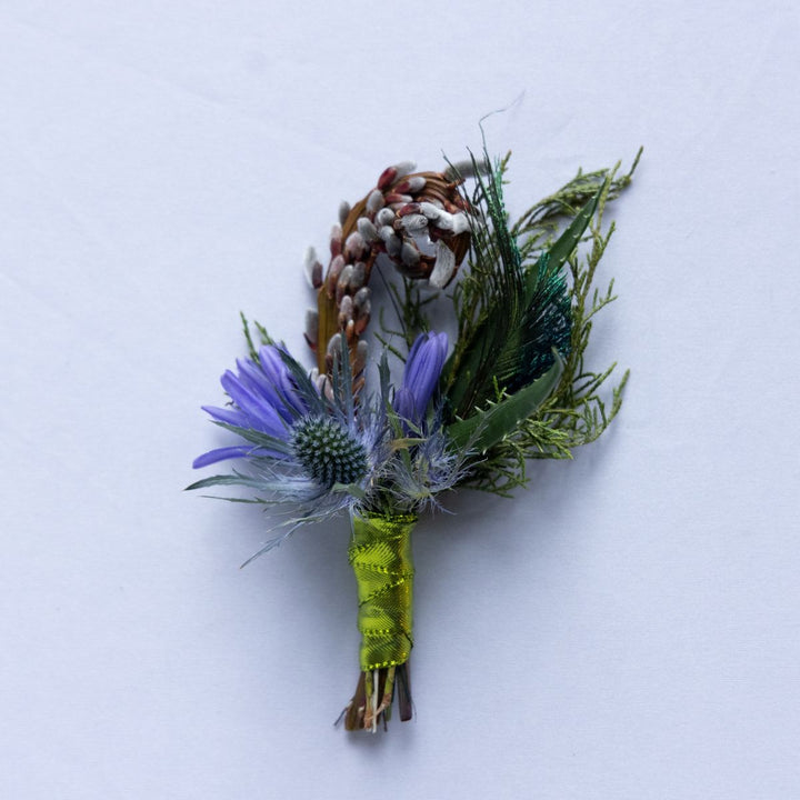 Floral boutonniere with purple flower and greenery on a white background