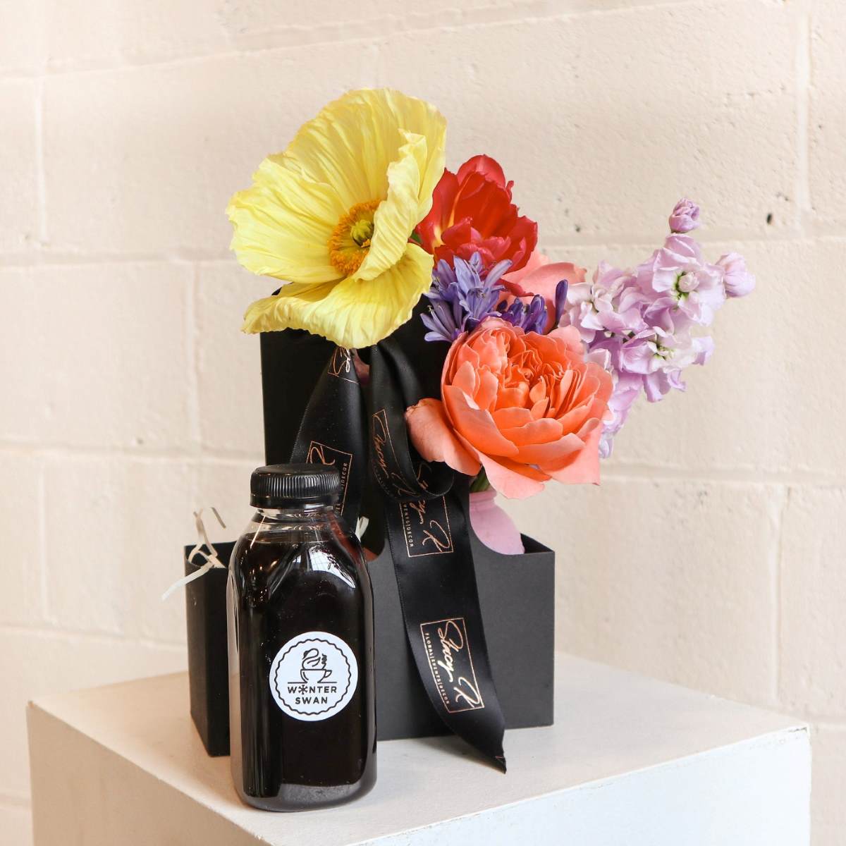 black gift box featuring a stunning arrangement of fresh flowers, including yellow poppy, peach rose, and lilac stock from stacy k floral  paired with a premium cold brew from winter swan coffee