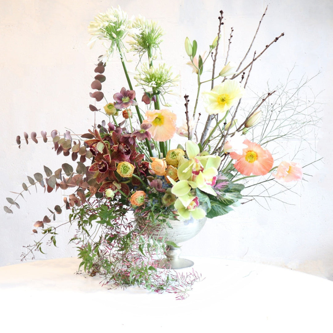 Springtime Majesty | A spring garden style with green, reds, pinks, yellows, and whites in a reflective vase. Photo taken against a white background. 