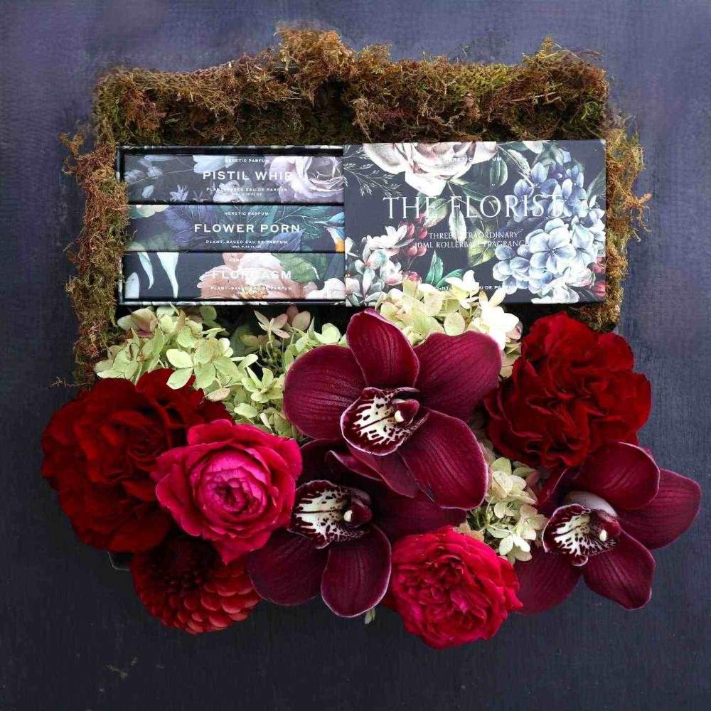 The Florist Gift Box | Stacy K Floral | A luxory gift box decorated with moss and filled with a red and green floral arrangement (featuring roses, hydrangea, orchids, and dahlias), and florist themed perfumes.