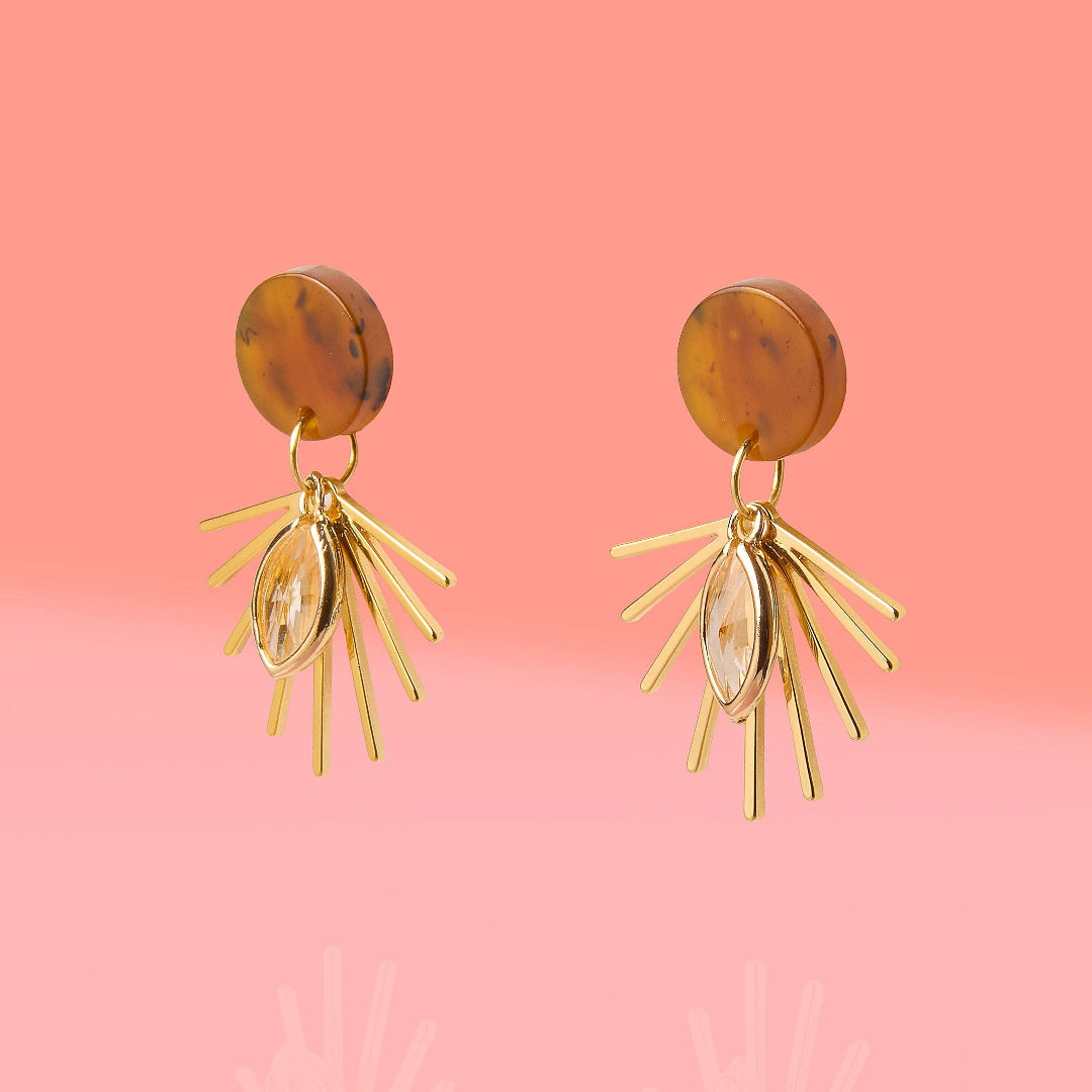 Gold earrings with brown circular tops on a pink background