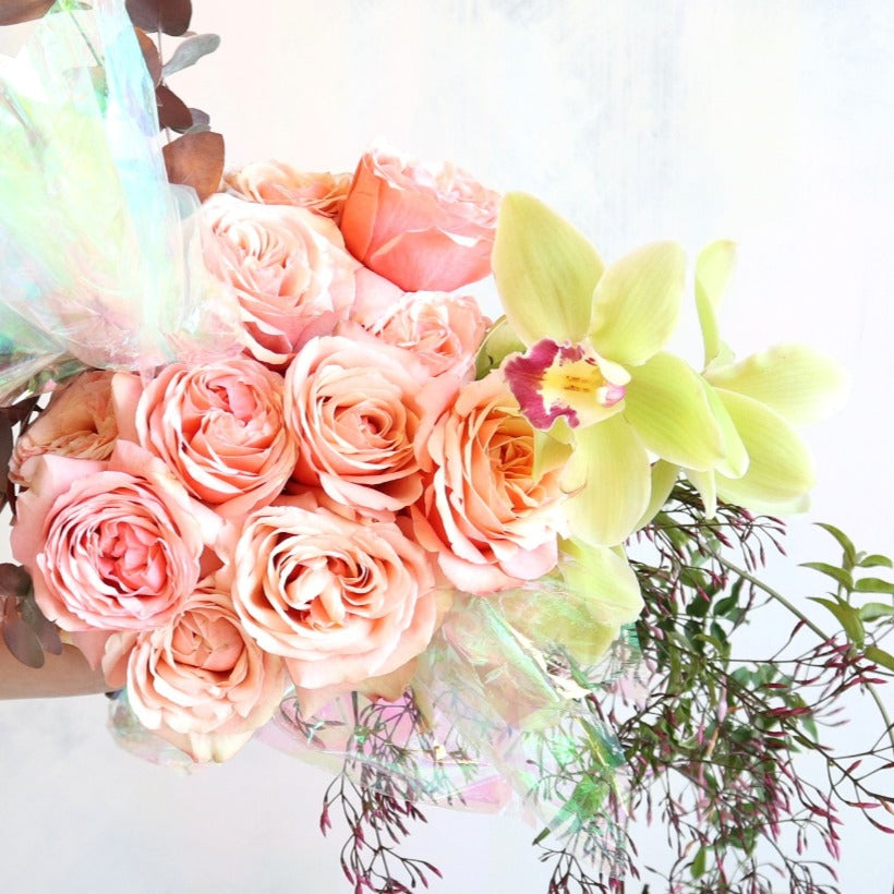 Peach roses, green orchids, greenery, and iridescent plastic.