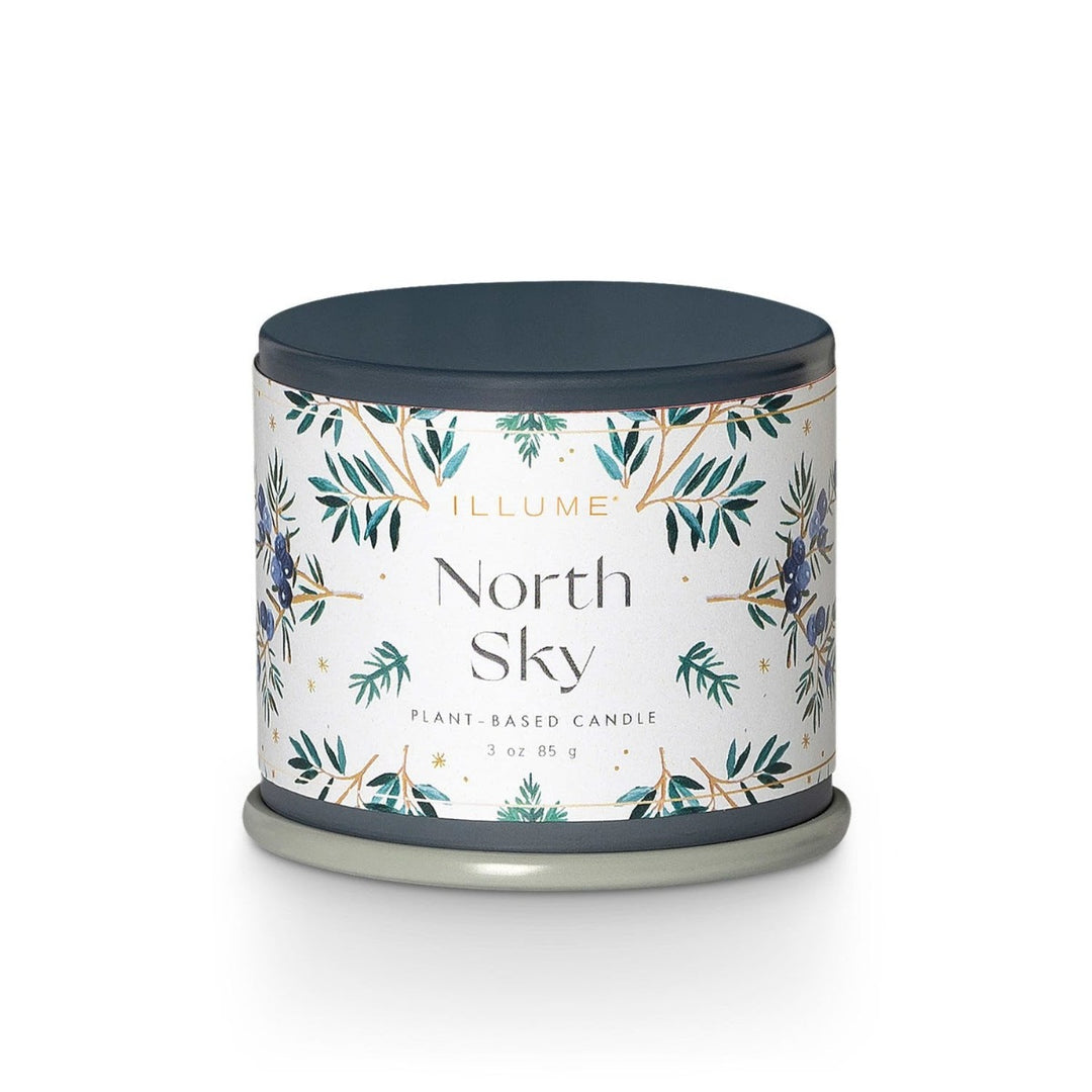 Illume Demi Tin Candle | North Sky | A blue tin with a white label decorated with leaves/branches, and blue berries. Label reads "Illume North Sky, plant based candle, 3 oz, 85g."