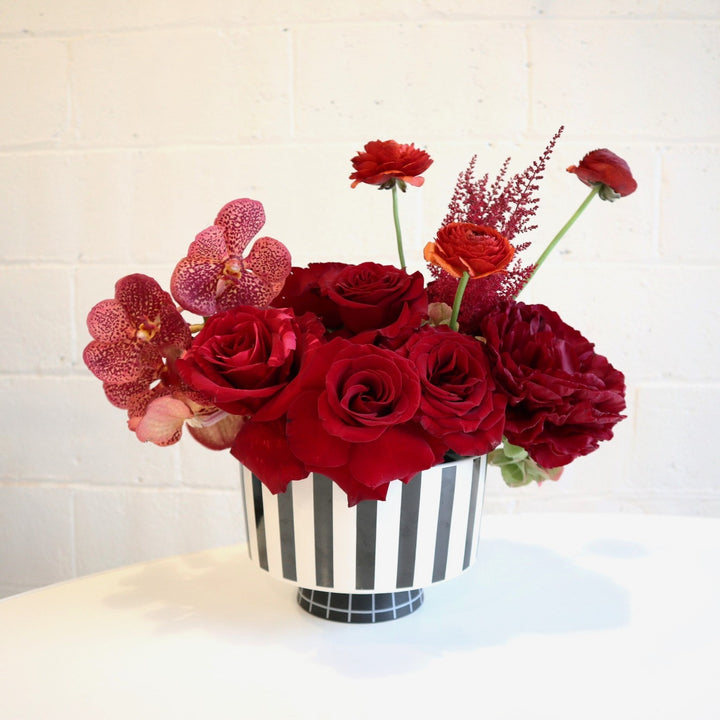 Ruby in Stripes | This elegant red beauty is made in a keepsake striped vessel. Flowers in photo include are red roses, orchids, peonies, ranunculus and hydrangea. 