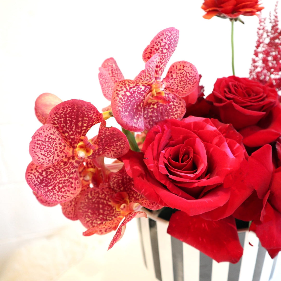Ruby in Stripes | close up of pink vanda orchids and red roses with a piece of the striped vase showing.