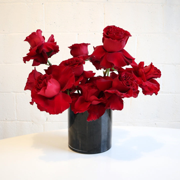 Red Rose Radiance| This arrangement filled with red roses, in a black vase on a white background.