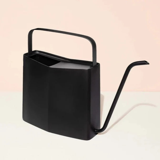 Matte Black Watering Can | Modern Sprout | A matte black watering can with a unique tapered square shape and a long spout. Photo taken against a pink/cream background.