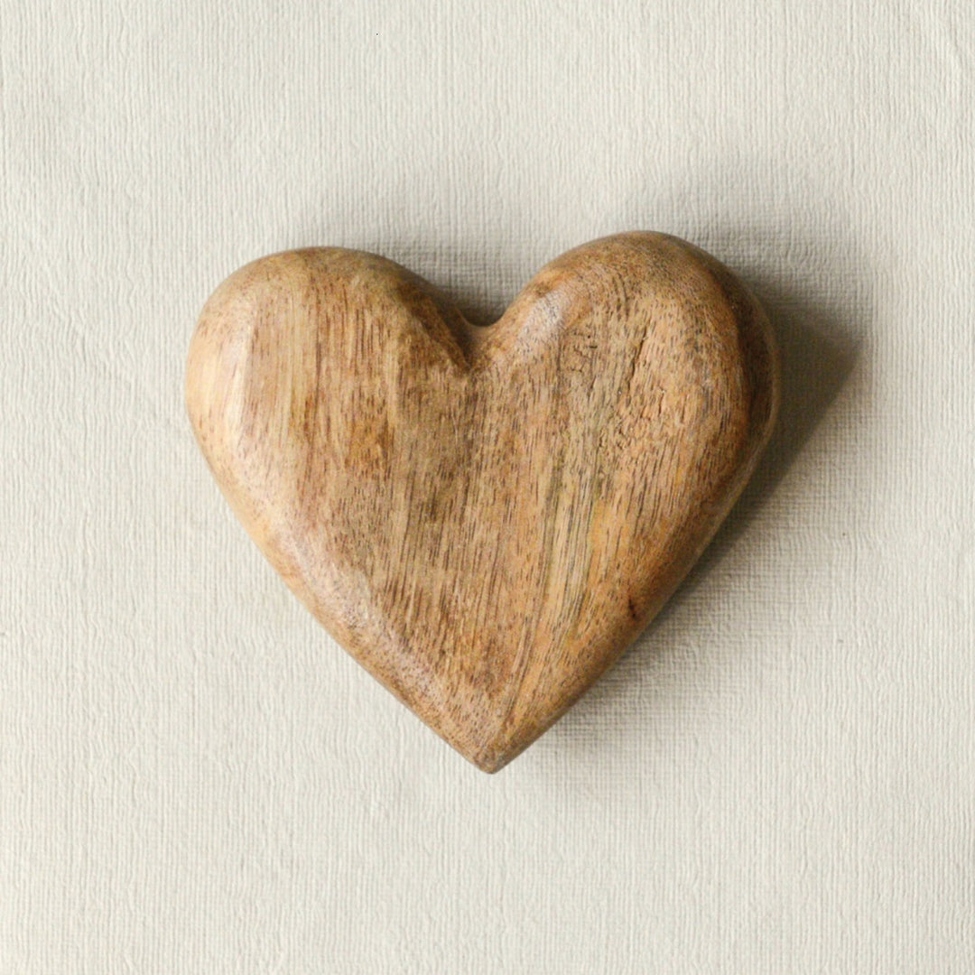 Hand-Carved Mango Wood Heart | A beautifully smooth, mango wood heart with little color variation and wood grain. Photo taken against textured paper.