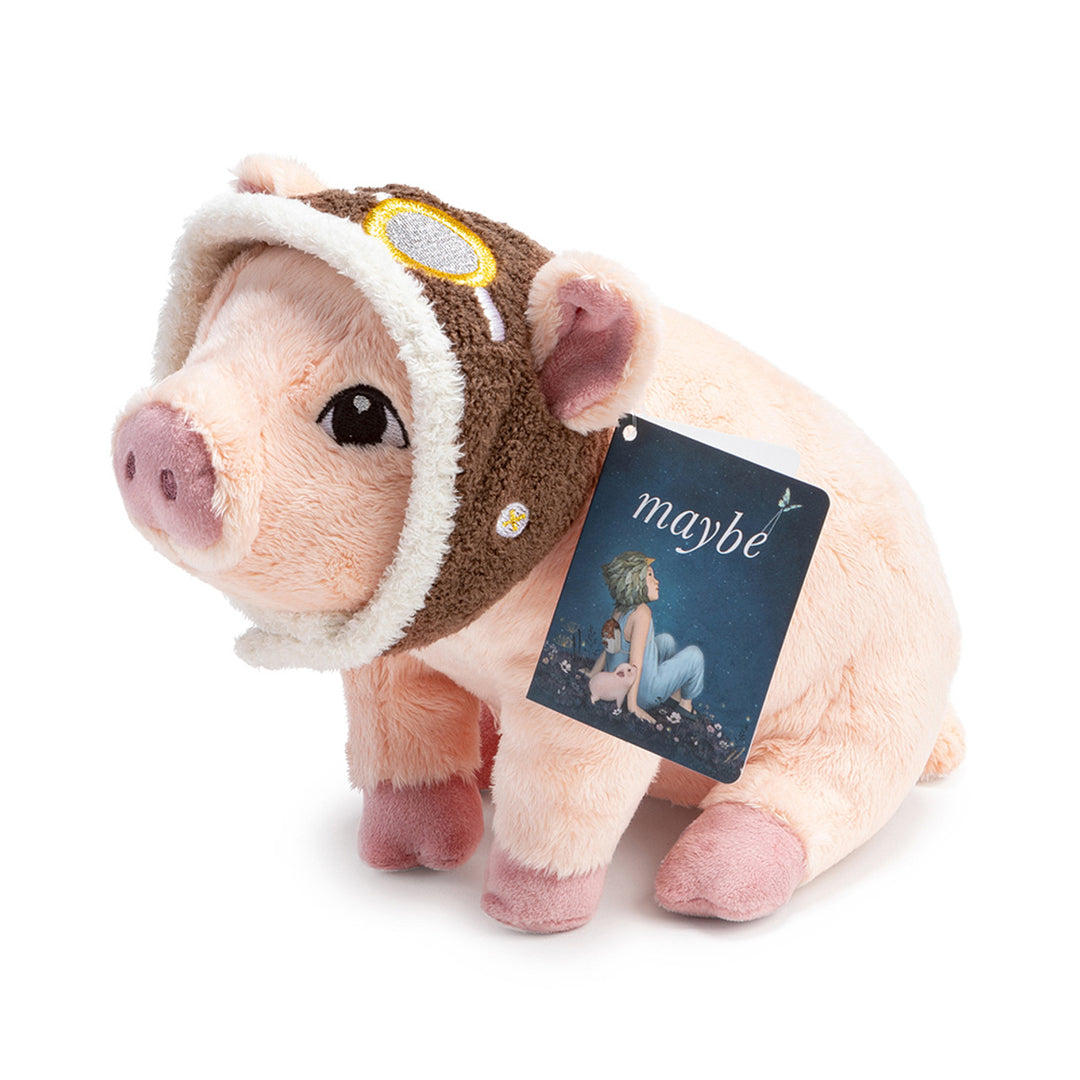 Flying Pig Plush | Pink pig plush with pilot's cap, camera is focusing in on the tag which is a tiny version of the "Maybe" children's picture book cover.