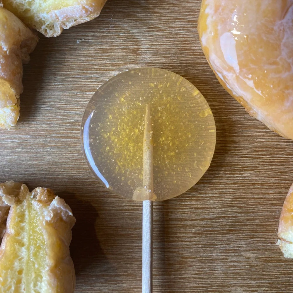 Good Lolli Lollipop Glazed Donut. Lollipop picture taken on a wooden background with glazed donuts placed around decoratively.