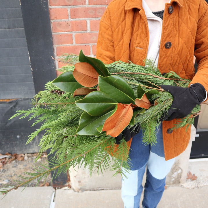 Bundle of evergreens and magnolia being held by a person with gloves on.