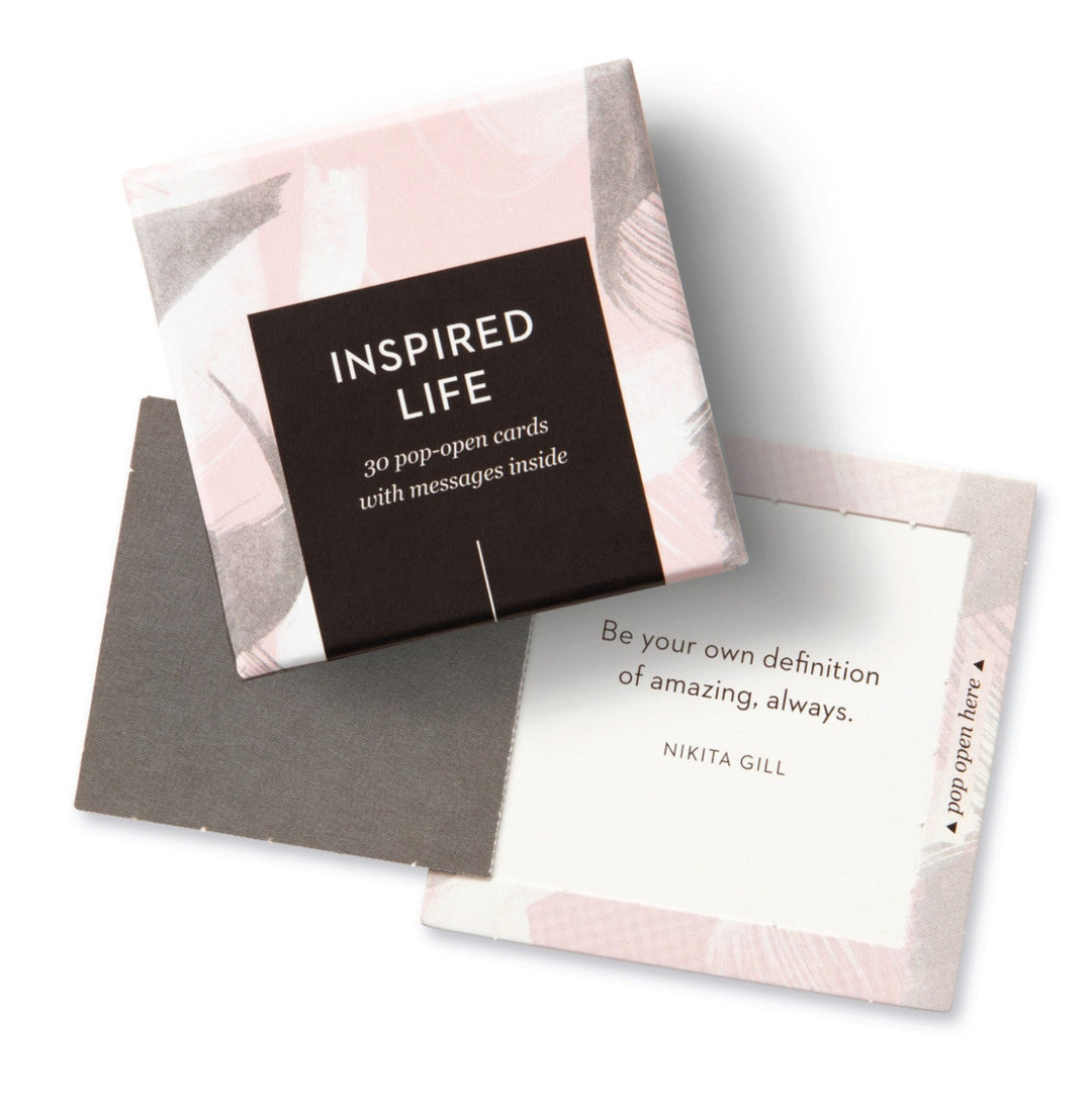 "An Inspired Life" Pop-Open Cards. A small box with in text "Inspired Life, 30 pop-open cards with messages inside, thoughtfuls". Box is decorated with pink, white, and black brush strokes. Open card is also displayed Photo taken against a white background.