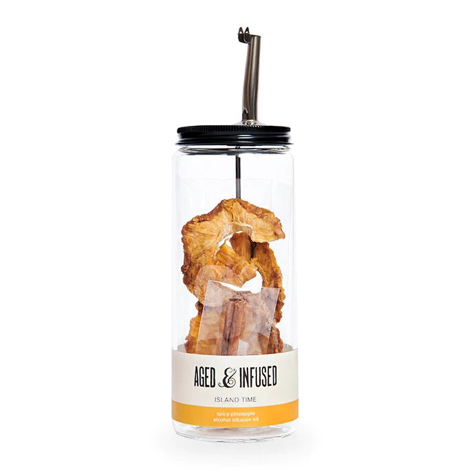 Aged & Infused Island Time | Alcohol infusion kit. Clear jar with dehydrated pineapple, and cinnamon visible through the glass. Black lid with pouring spout.