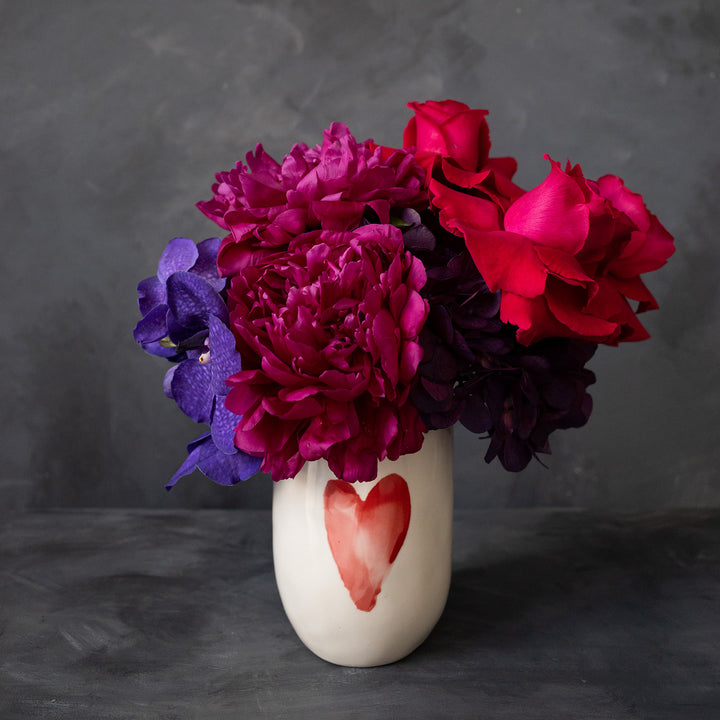 Jewel tone blooms in a water color heart vase with a grey backdrop.  Valentines day Flower delivery | Rochester NY Florist