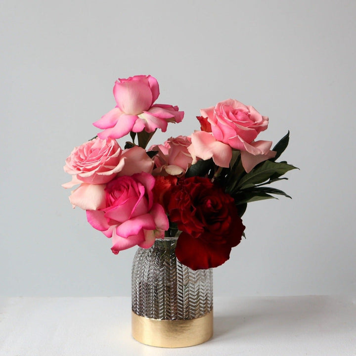 A variety of pink roses in different shades of pink, designed in an clear glass vase with gold bottom.