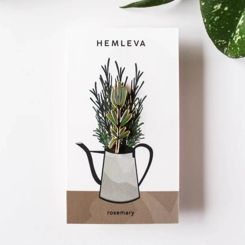 Hemleva Enamel Pins | Green rosemary shaped pin in packaging that is decorated with a watering can filled with rosemary.
