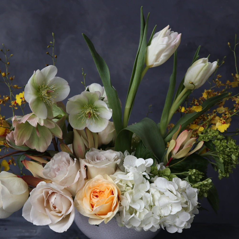 Spring floral arrangement with white and green hydrangea, white tulips, light roses, and yellow accents. Photo taken on dark backdrop.