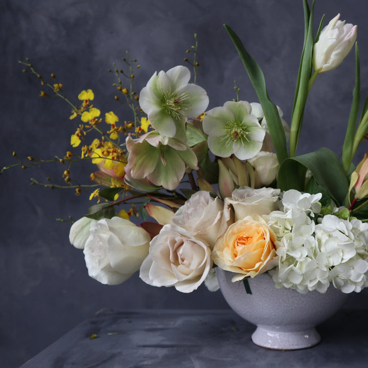 Spring floral arrangement with white and green hydrangea, white tulips, light roses, and yellow accents. Photo taken on dark backdrop.