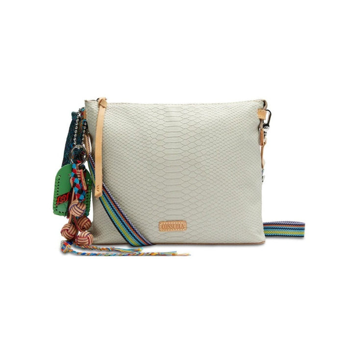 Thunderbird Downtown Crossbody | Consuela | A light gray/cream rattlesnake pattern bag with nude accents and a colorful keepsakes/keychains hanging on the left side. Crossbody strap is striped multicolor.