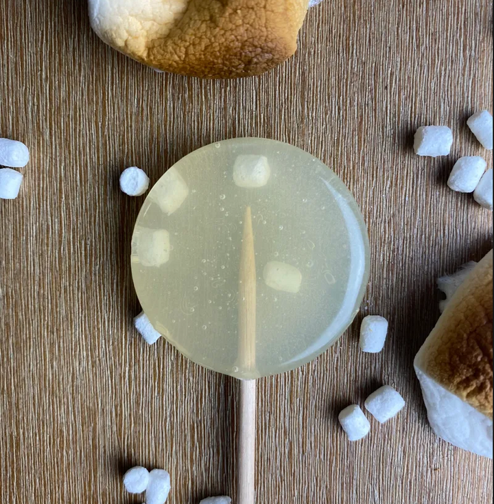 Good Lolli Lollipops | Toasted Marshmallow | A transparent lolli with mini marshmallows inside. Toasted marshmallows and tiny marshmallows strewn about.
