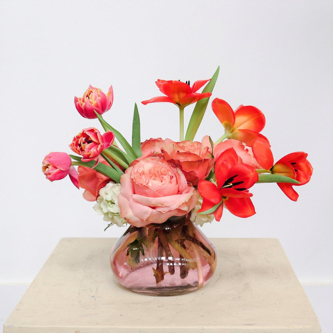 Tulips and Roses | A pink and red arrangement with double tulips, roses, and  hydrangea in a transparent pink vase.