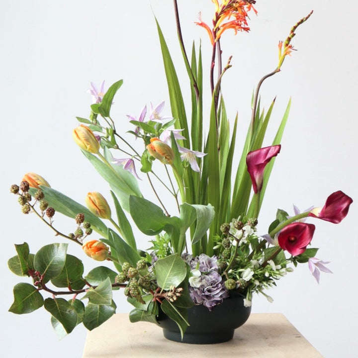 Spring Fountain | A floral arrangement made with blooms such as tulips, calla lilies, carnations and an assortment of other spring flowers. The colors are green, orange, magenta, and lilac. Close up on the arrangement.